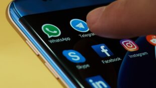 Närbild på ett pekfinger och en mobilskärm med flera ikoner för appar, däribland Telegram.