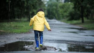 barn i gul regnjacka plaskar i vattenpöl.