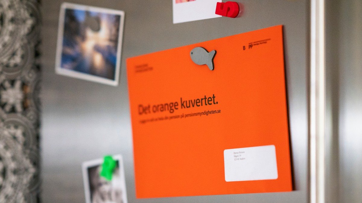 Grå kylskåpsdörr där ett orange kuvert sitter fast med en magnet.