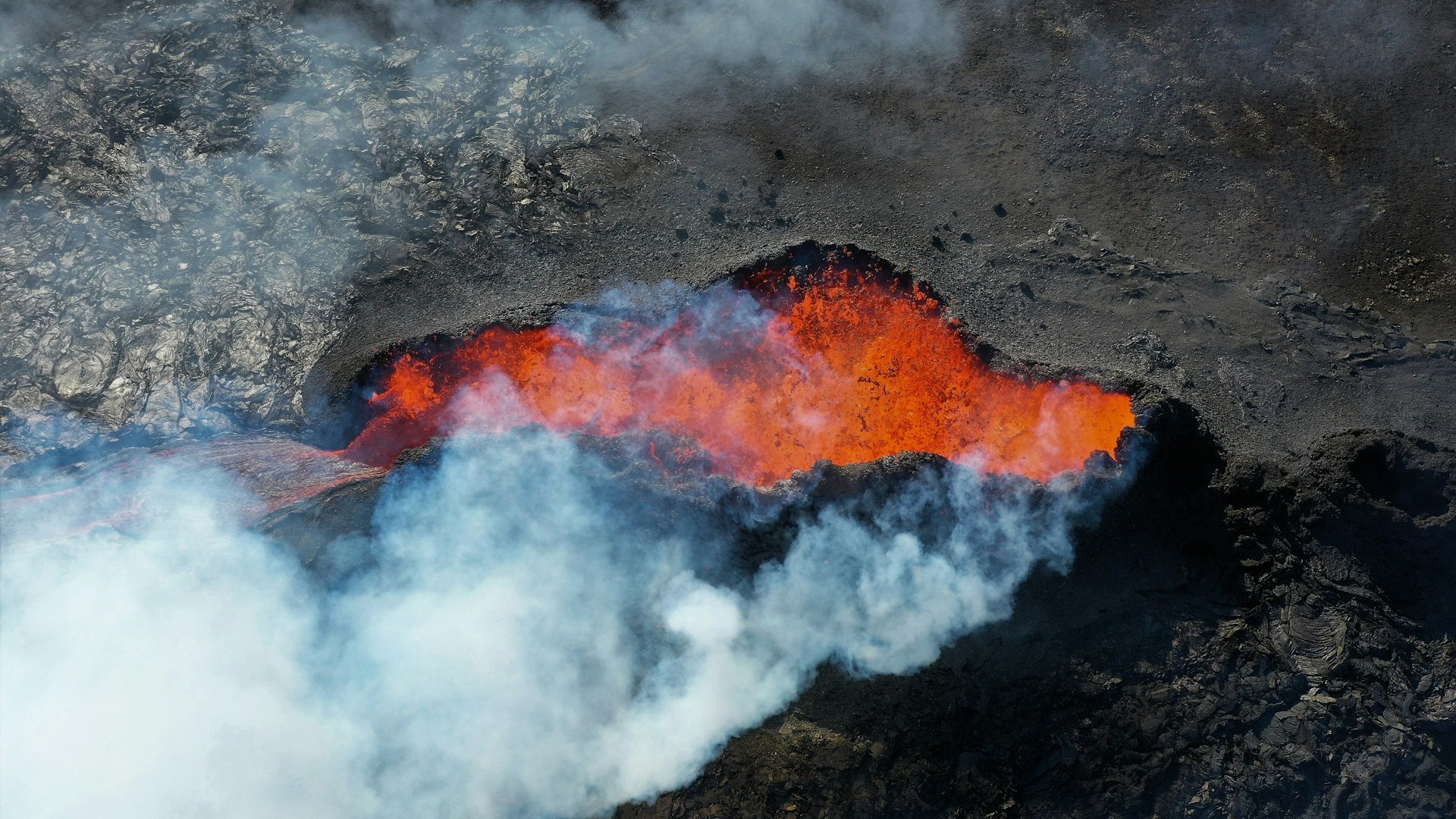 Vulkankrater med röd lava och vit rök som strömmar ut.