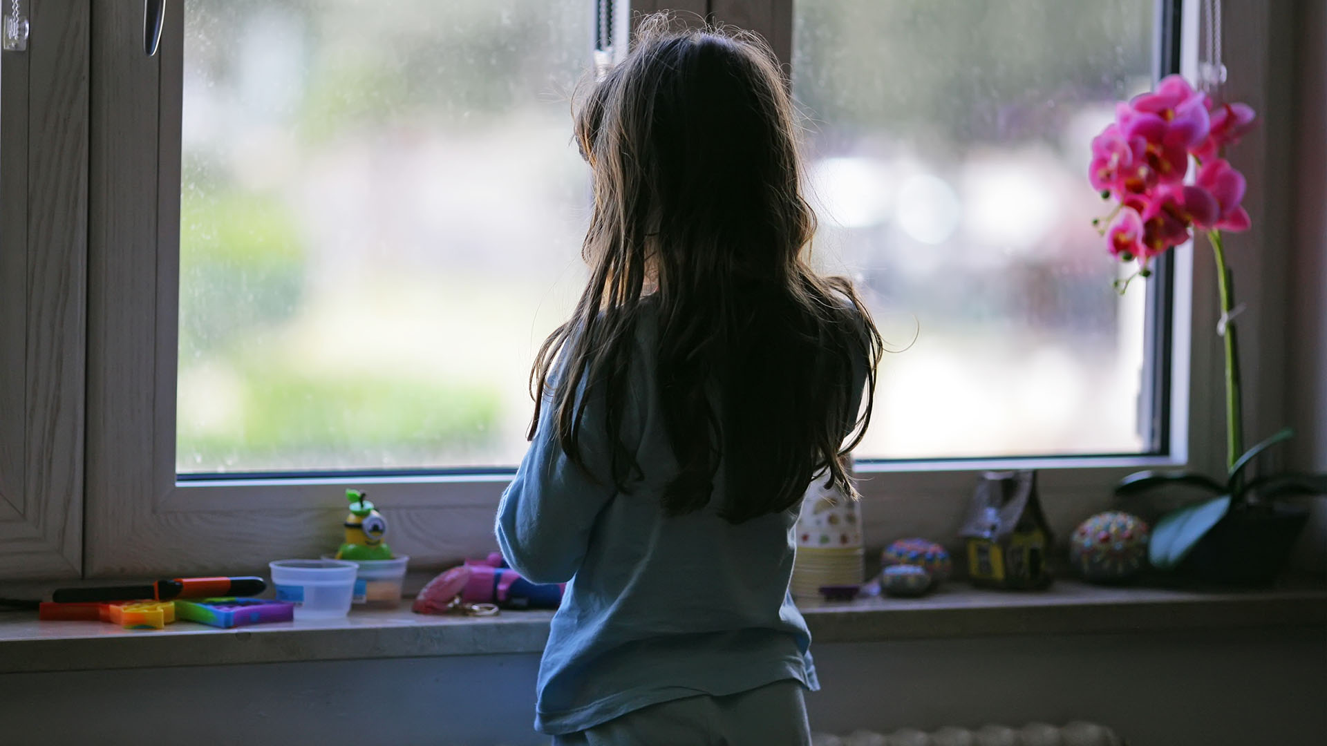 Ensam flicka i barnrum tittar ut genom fönster.