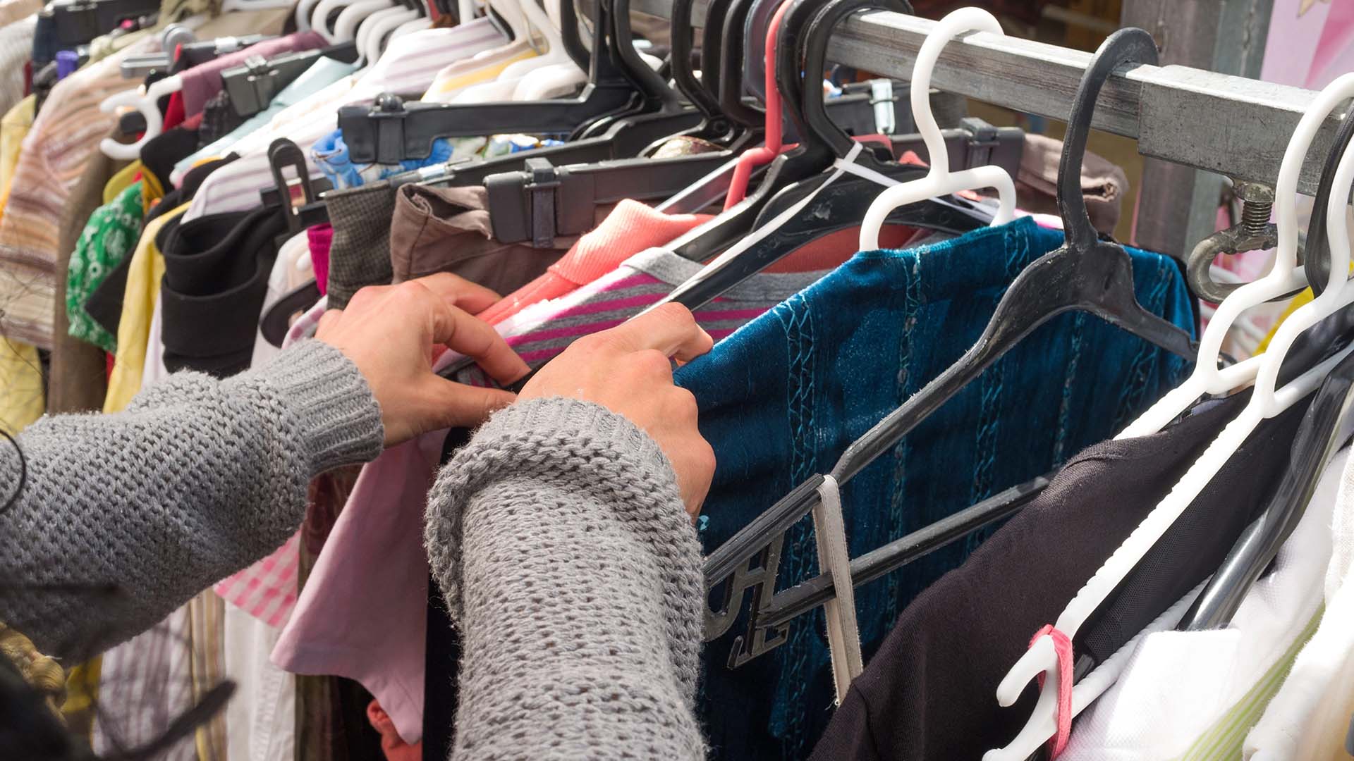 Kvinna letar kläder som hänger på galgar i en butik.