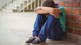 Ensam pojke sitter intill tegelvägg