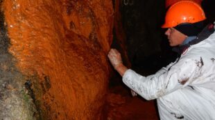 Forskare med handske tar prover på en vägg med roströd biofilm.