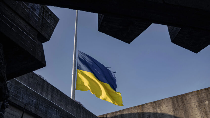 En sliten ukrainsk flagga siktas mellan konturer av en byggnad.