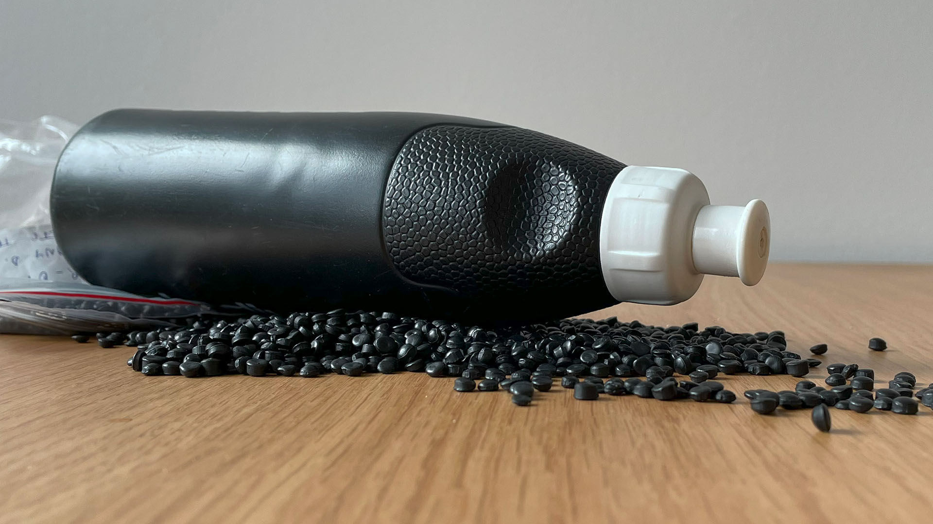 Svart plastflaska och pellets på ett bord.