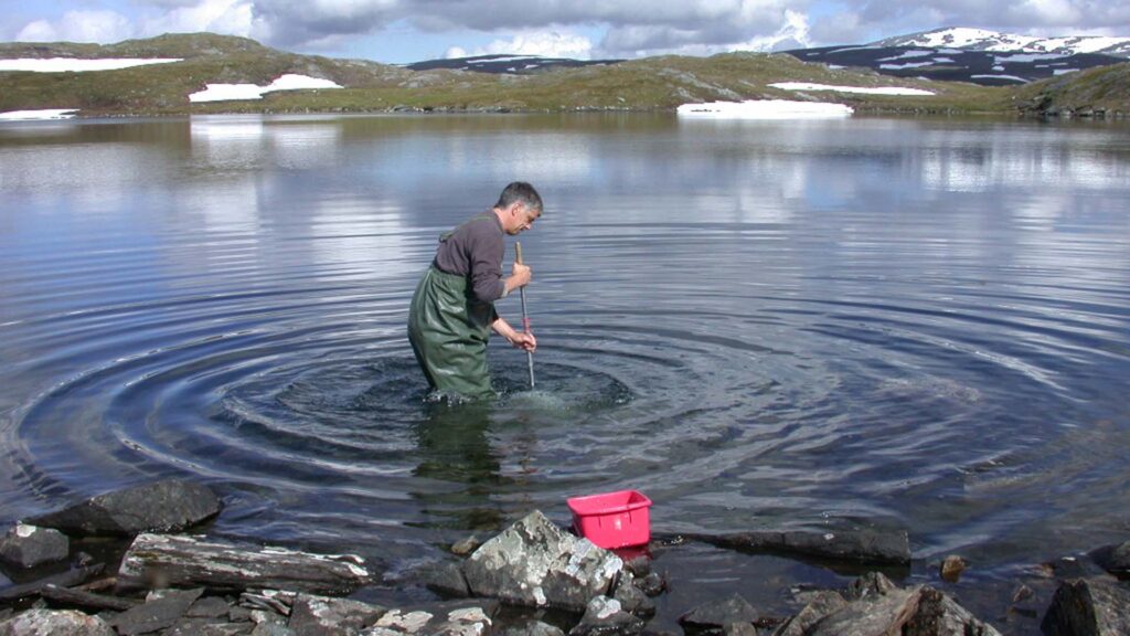 Forskare samlar in prover. I bakgrunden ses fjällandskap med berg.