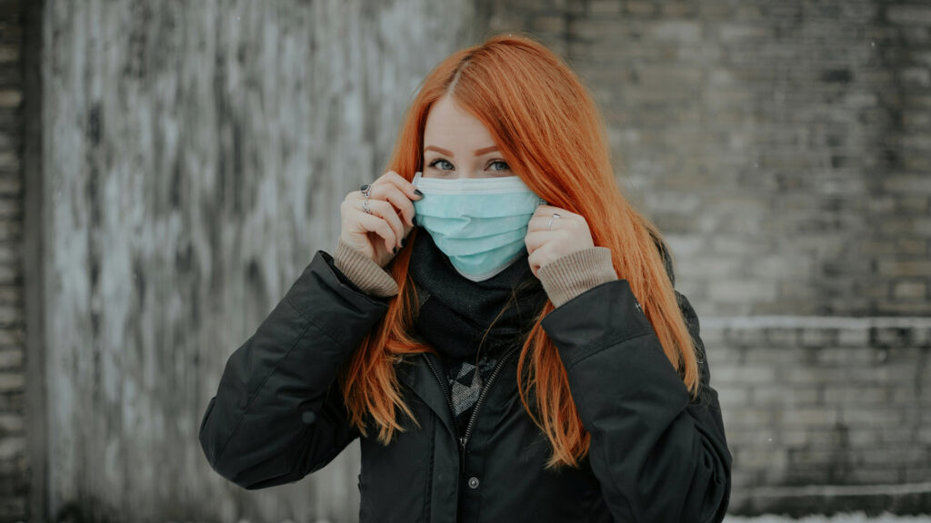 Kvinna med långt rött tar på sig ett blått munskydd.
