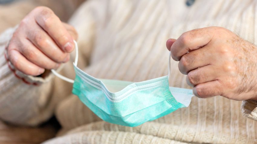 Äldre person håller i ett munskydd.